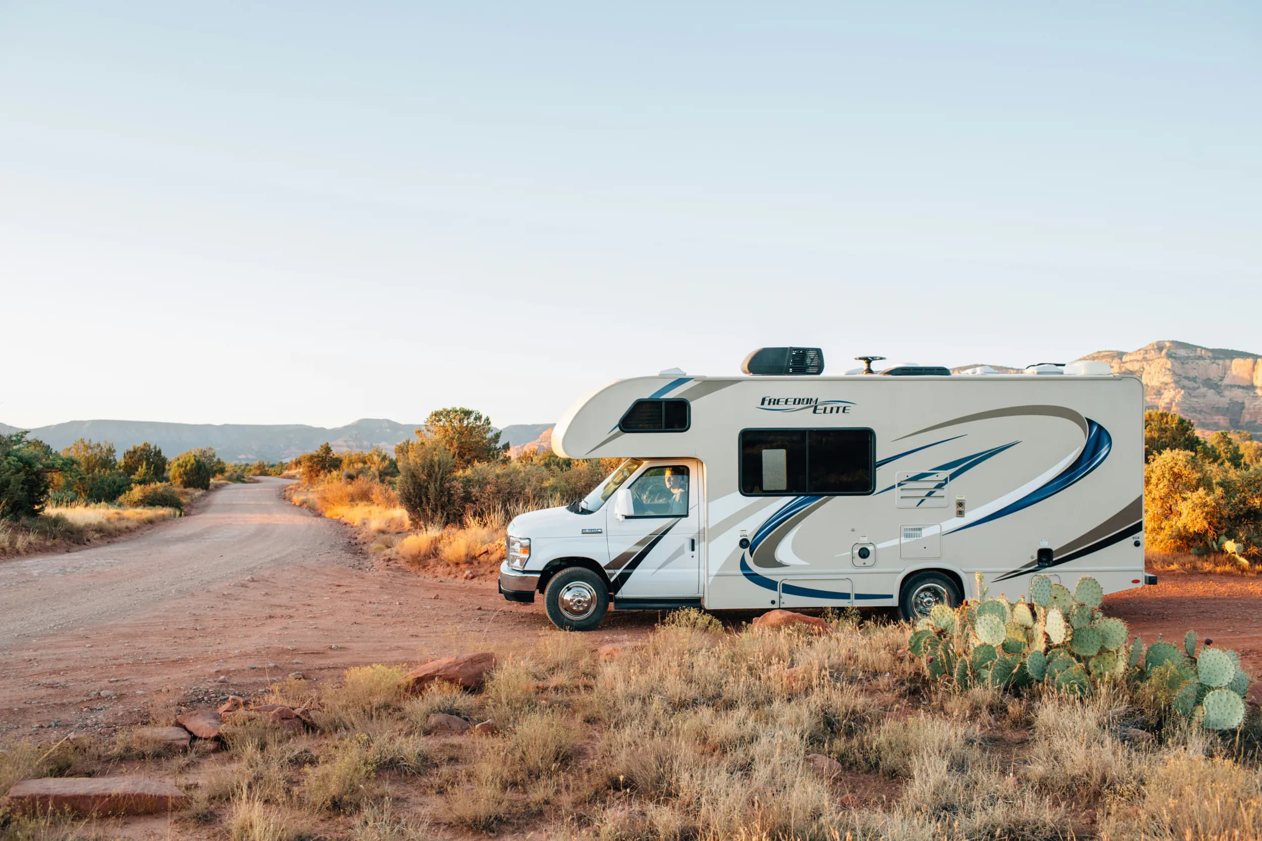A motorhome parked beside a dirt road in the desert at golden hour