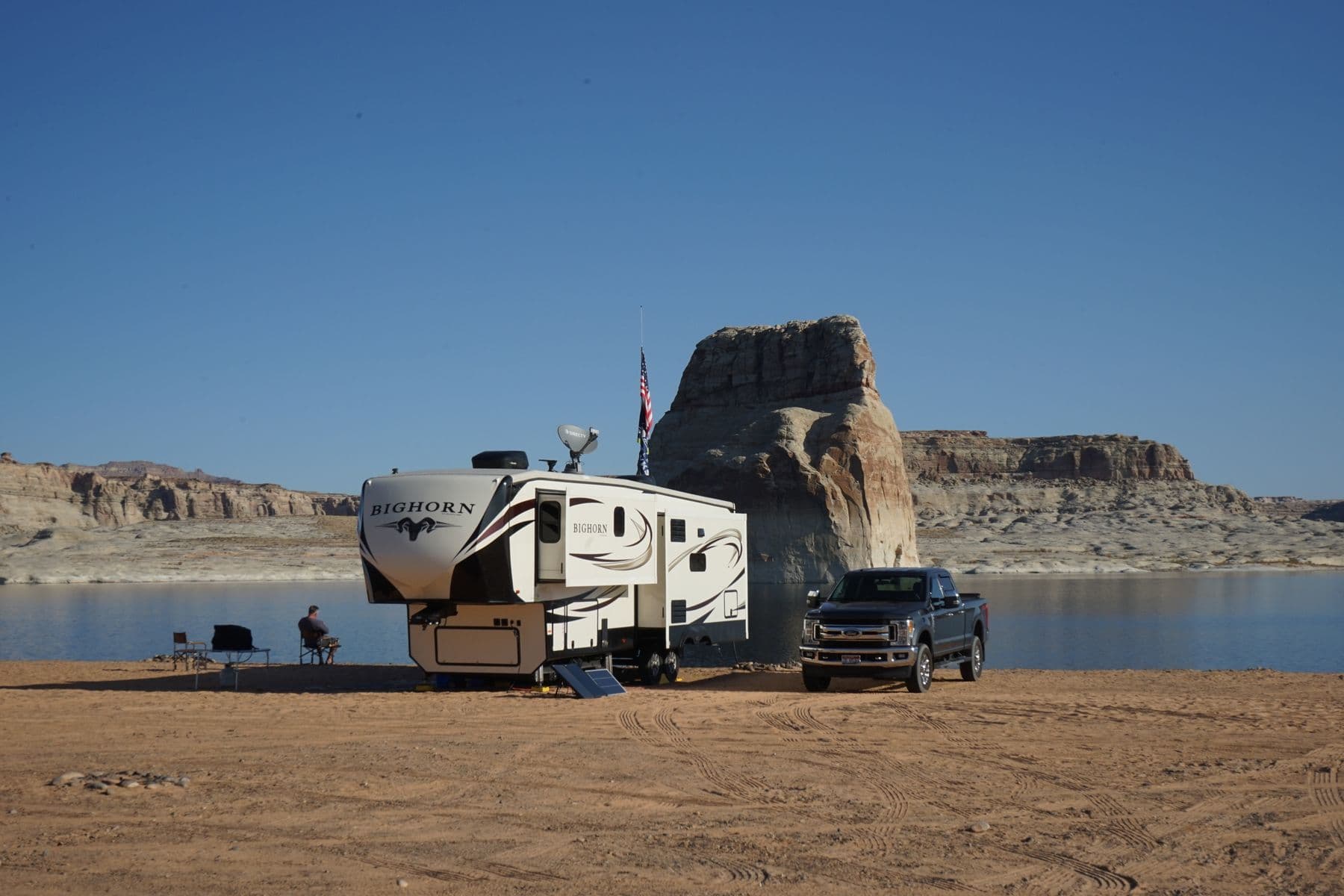 A fifth-wheel trailer and a pickup truck parked on the shore of a desert lake
